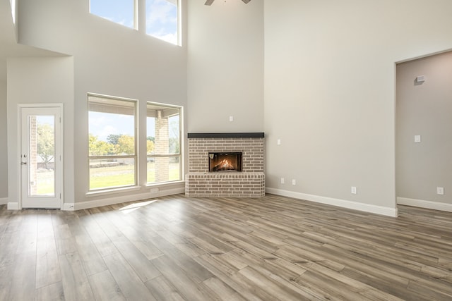 unfurnished living room featuring a high ceiling, ceiling fan, a brick fireplace, and light hardwood / wood-style flooring