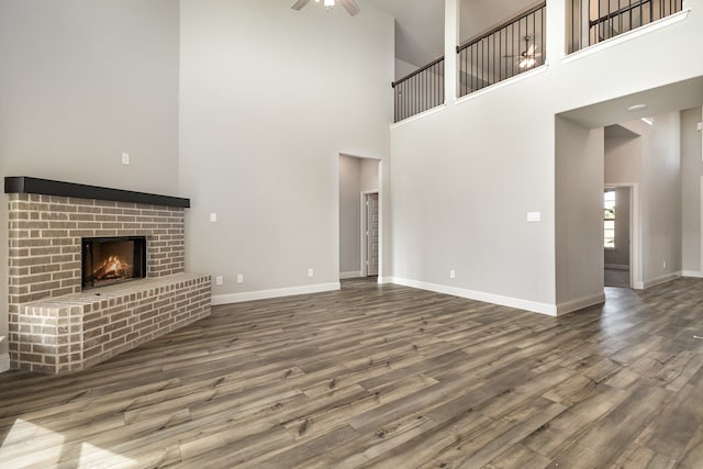 unfurnished living room with ceiling fan, a high ceiling, wood-type flooring, and a brick fireplace