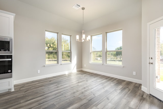 unfurnished dining area featuring hardwood / wood-style floors, a healthy amount of sunlight, and a chandelier