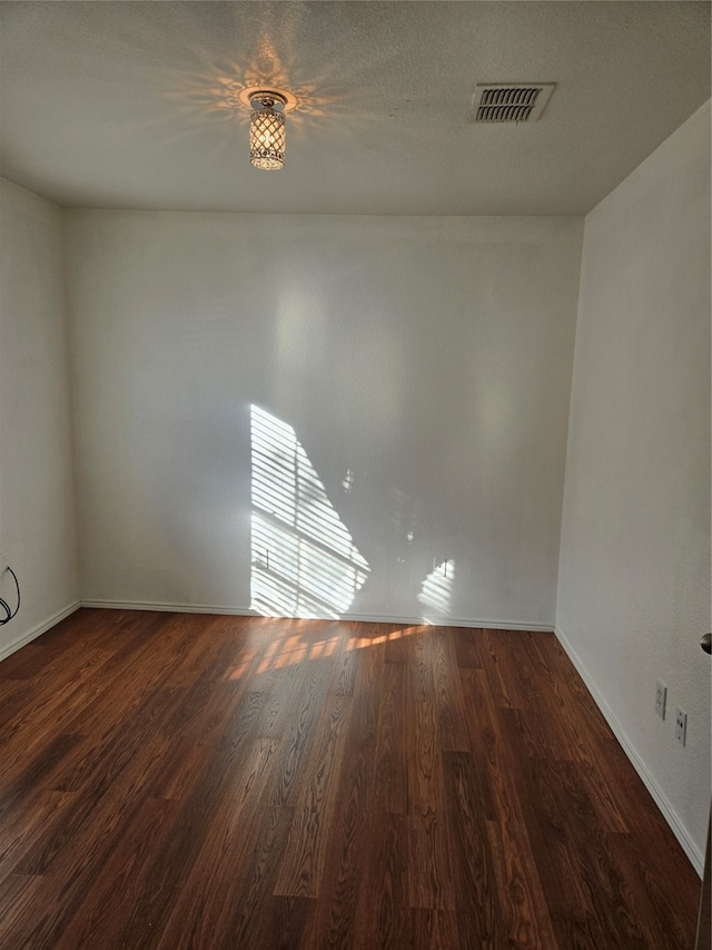 spare room featuring dark wood-type flooring and a textured ceiling