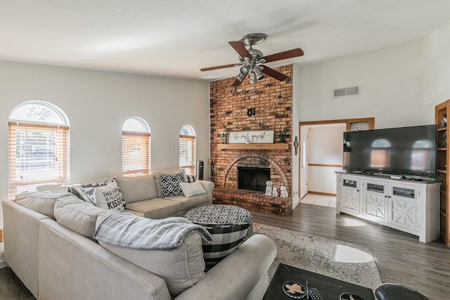 living room with dark wood-type flooring, a towering ceiling, ceiling fan, and a brick fireplace