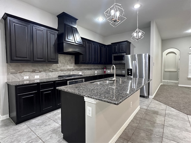 kitchen featuring stainless steel appliances, dark stone counters, sink, tasteful backsplash, and a kitchen island with sink