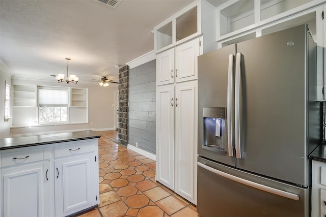 kitchen with wood walls, stainless steel fridge, hanging light fixtures, and white cabinets