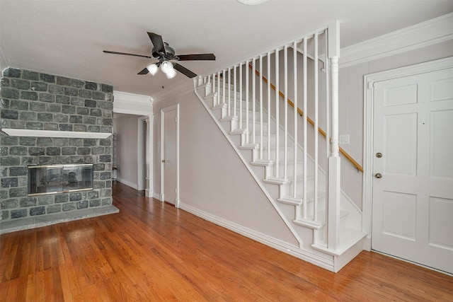 unfurnished living room with ceiling fan, ornamental molding, wood-type flooring, and a fireplace