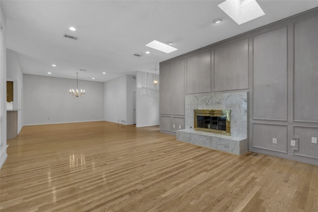 unfurnished living room featuring light wood-type flooring, a chandelier, a fireplace, and a skylight