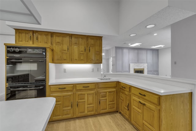 kitchen with a peninsula, a sink, light countertops, dobule oven black, and light wood-type flooring