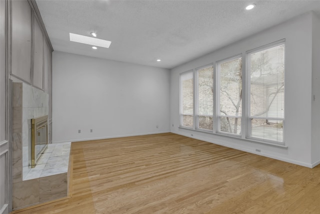 unfurnished living room with a textured ceiling, a skylight, a fireplace, and light wood finished floors