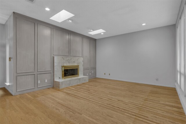 unfurnished living room with baseboards, light wood-type flooring, recessed lighting, a fireplace, and a skylight