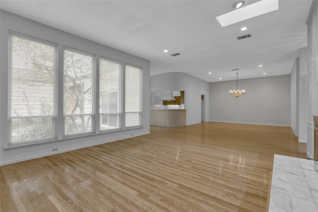 unfurnished living room featuring a wealth of natural light, visible vents, a notable chandelier, and a skylight