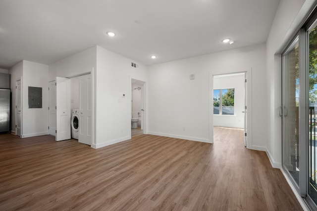 unfurnished living room with washer / clothes dryer, electric panel, and light hardwood / wood-style floors