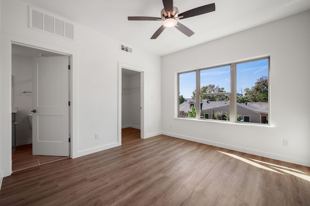 unfurnished bedroom with a spacious closet, dark hardwood / wood-style floors, ceiling fan, and a closet