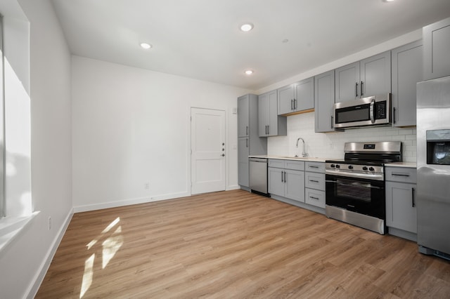 kitchen featuring stainless steel appliances, light wood-type flooring, gray cabinets, sink, and decorative backsplash