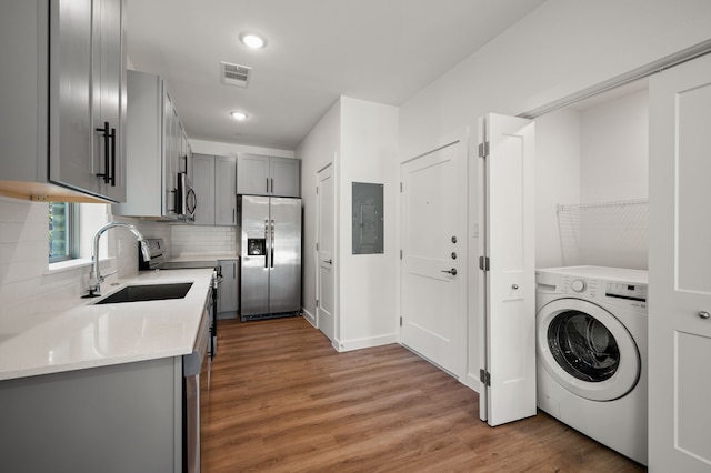 kitchen with gray cabinetry, stainless steel appliances, washer / clothes dryer, sink, and hardwood / wood-style floors