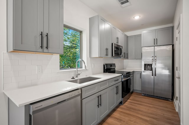 kitchen with tasteful backsplash, stainless steel appliances, gray cabinets, sink, and hardwood / wood-style flooring