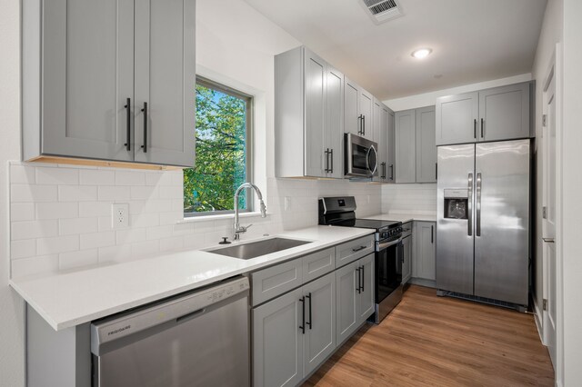 kitchen with tasteful backsplash, stainless steel appliances, gray cabinets, sink, and hardwood / wood-style flooring