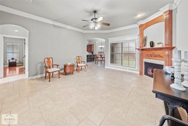 living area with a fireplace, ceiling fan with notable chandelier, and crown molding