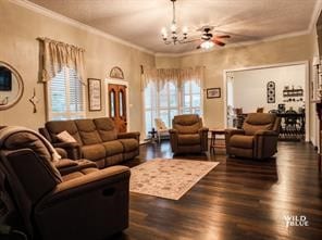 living room featuring dark hardwood / wood-style flooring, ceiling fan with notable chandelier, and crown molding