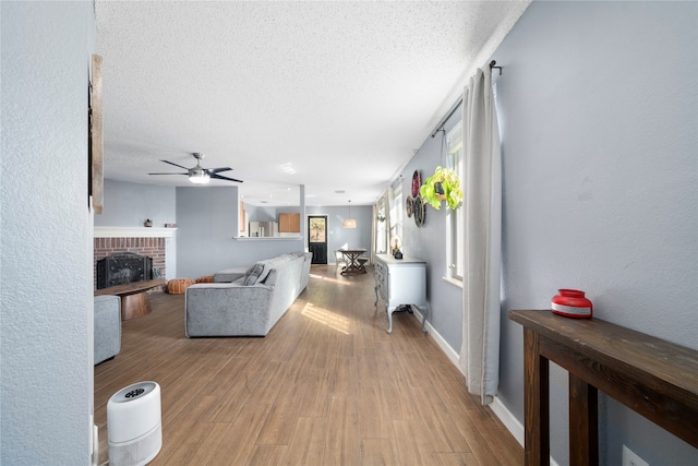 living room with hardwood / wood-style flooring, ceiling fan, a textured ceiling, and a brick fireplace