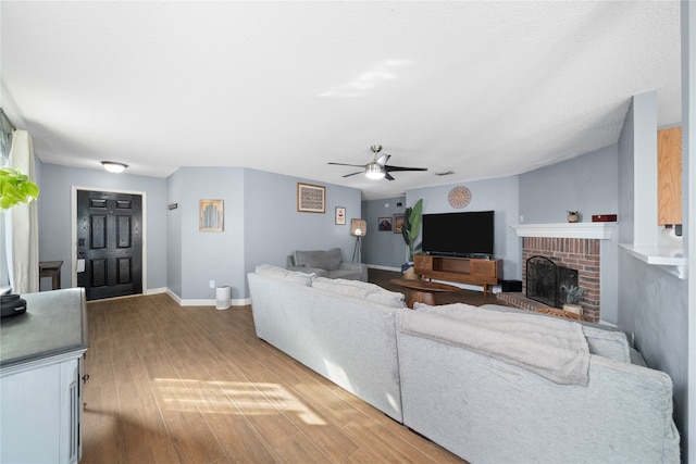 living room featuring ceiling fan, wood-type flooring, and a brick fireplace