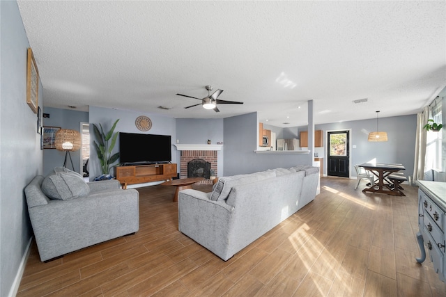 living room with ceiling fan, hardwood / wood-style floors, a textured ceiling, and a brick fireplace