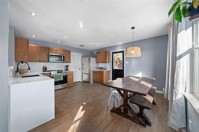 kitchen featuring appliances with stainless steel finishes, a textured ceiling, dark wood-type flooring, sink, and decorative light fixtures