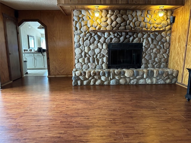 unfurnished living room with a stone fireplace, wood walls, and wood-type flooring