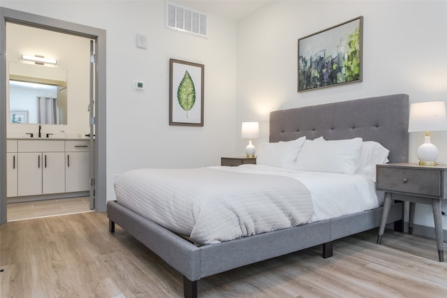 bedroom with light wood-type flooring, sink, and ensuite bath