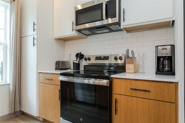 kitchen with light hardwood / wood-style flooring, tasteful backsplash, white cabinetry, and stainless steel appliances