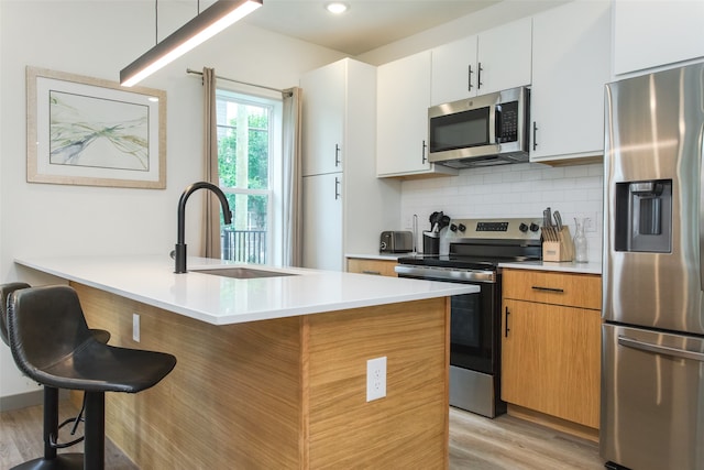 kitchen with stainless steel appliances, white cabinets, sink, a kitchen breakfast bar, and light wood-type flooring