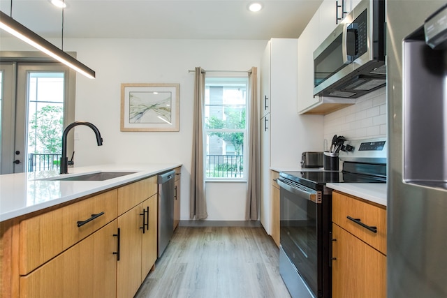 kitchen with stainless steel appliances, white cabinets, sink, backsplash, and light wood-type flooring