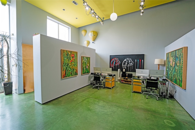 office space featuring concrete floors, a towering ceiling, and rail lighting