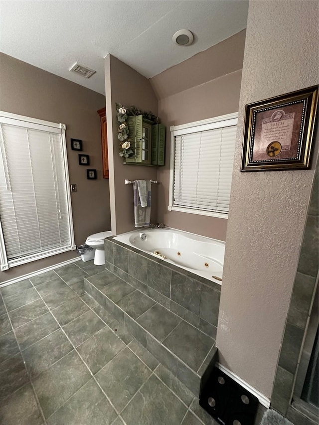 full bathroom with visible vents, a textured wall, toilet, vaulted ceiling, and a whirlpool tub