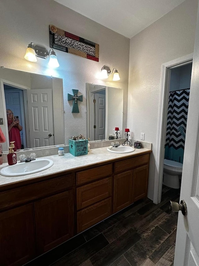 bathroom featuring double vanity, wood finished floors, a sink, and toilet