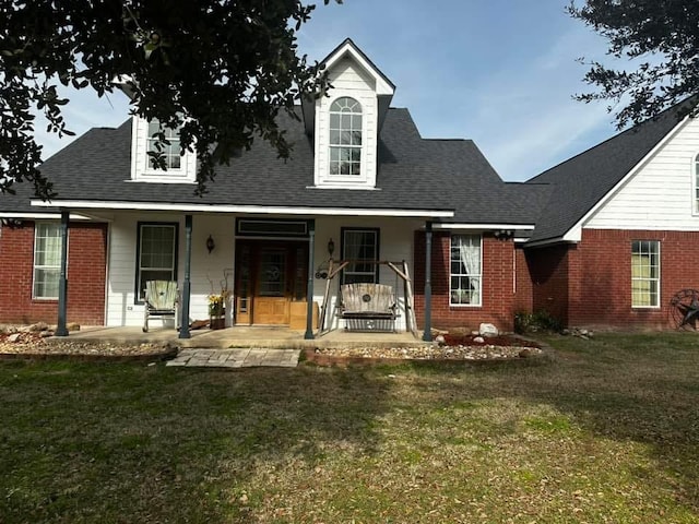 new england style home featuring a porch, brick siding, a shingled roof, and a front lawn