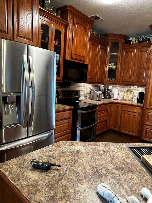 kitchen with tasteful backsplash, visible vents, glass insert cabinets, stainless steel appliances, and a textured ceiling