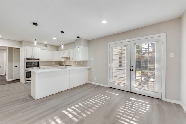 kitchen with kitchen peninsula, hanging light fixtures, stainless steel double oven, light hardwood / wood-style flooring, and white cabinets