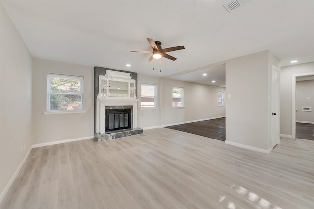 unfurnished living room featuring a premium fireplace, light hardwood / wood-style flooring, and ceiling fan