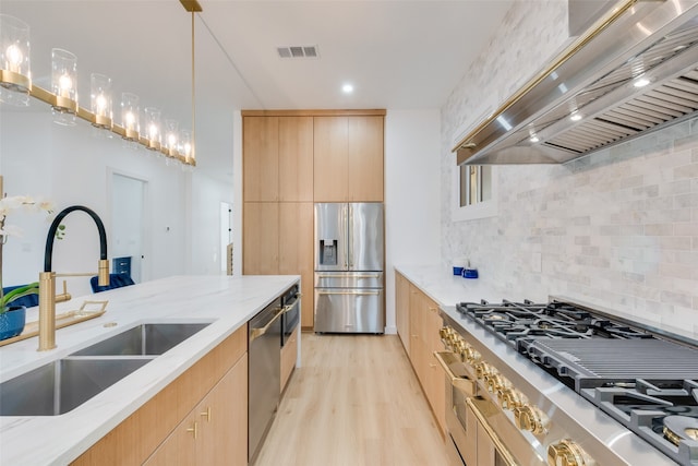 kitchen with stainless steel appliances, light stone counters, custom exhaust hood, hanging light fixtures, and light hardwood / wood-style flooring