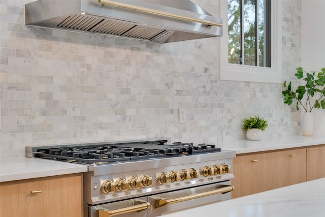 kitchen with wall chimney range hood, stainless steel gas stove, and tasteful backsplash