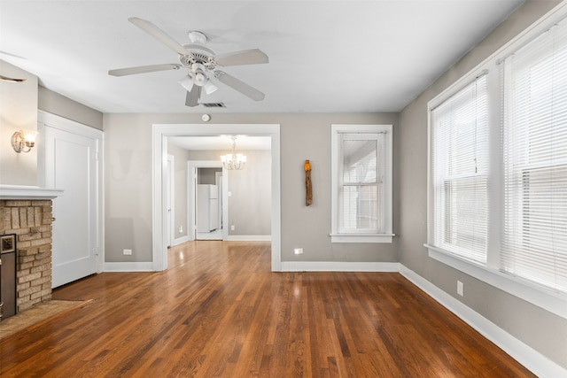 unfurnished living room with a fireplace, dark hardwood / wood-style floors, a healthy amount of sunlight, and ceiling fan with notable chandelier