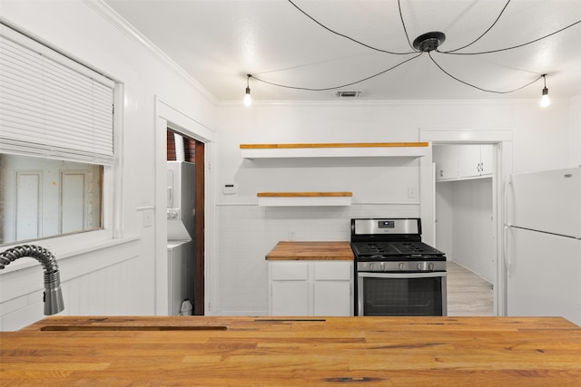 kitchen featuring stacked washing maching and dryer, butcher block countertops, white fridge, stainless steel gas range, and white cabinetry