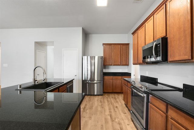 kitchen with dark stone counters, light hardwood / wood-style flooring, stainless steel appliances, and sink