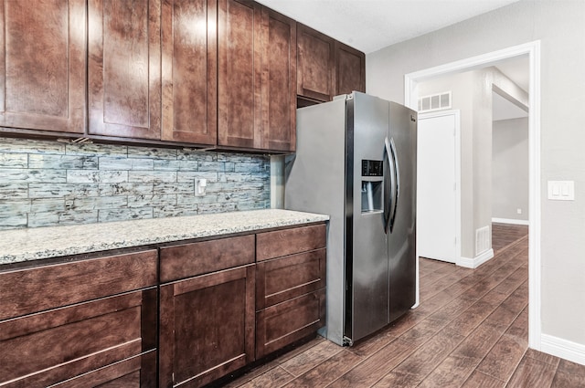 kitchen featuring light stone counters, stainless steel refrigerator with ice dispenser, backsplash, dark brown cabinets, and dark hardwood / wood-style flooring