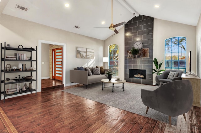 living room with dark wood-type flooring, a tile fireplace, high vaulted ceiling, ceiling fan, and beam ceiling