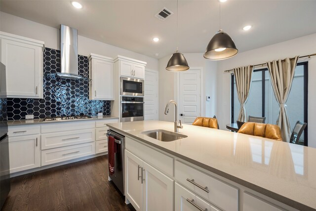 kitchen featuring stainless steel appliances, sink, wall chimney exhaust hood, decorative light fixtures, and white cabinets