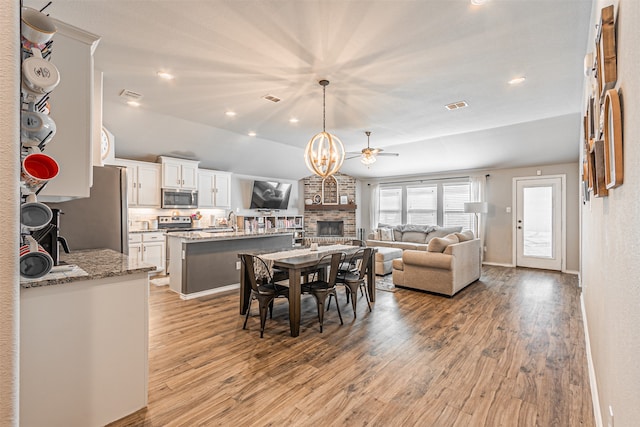 dining room with ceiling fan, a stone fireplace, sink, and light wood-type flooring