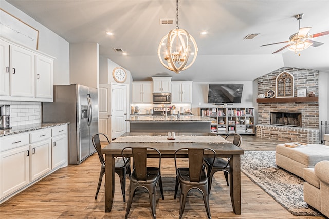 dining area featuring a fireplace, light hardwood / wood-style flooring, lofted ceiling, and ceiling fan with notable chandelier