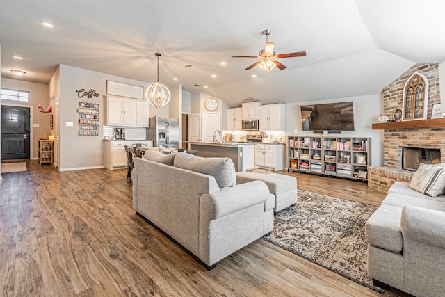 living room with hardwood / wood-style floors, a fireplace, sink, and vaulted ceiling