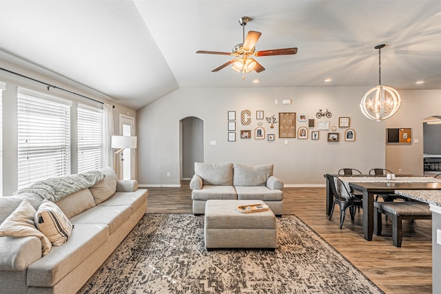 living room with ceiling fan with notable chandelier, hardwood / wood-style flooring, and vaulted ceiling