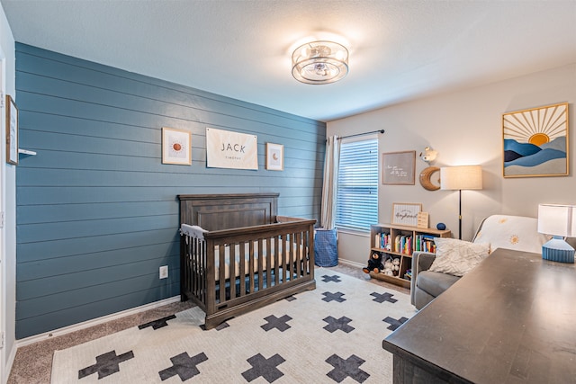 carpeted bedroom featuring a crib, a textured ceiling, and wooden walls